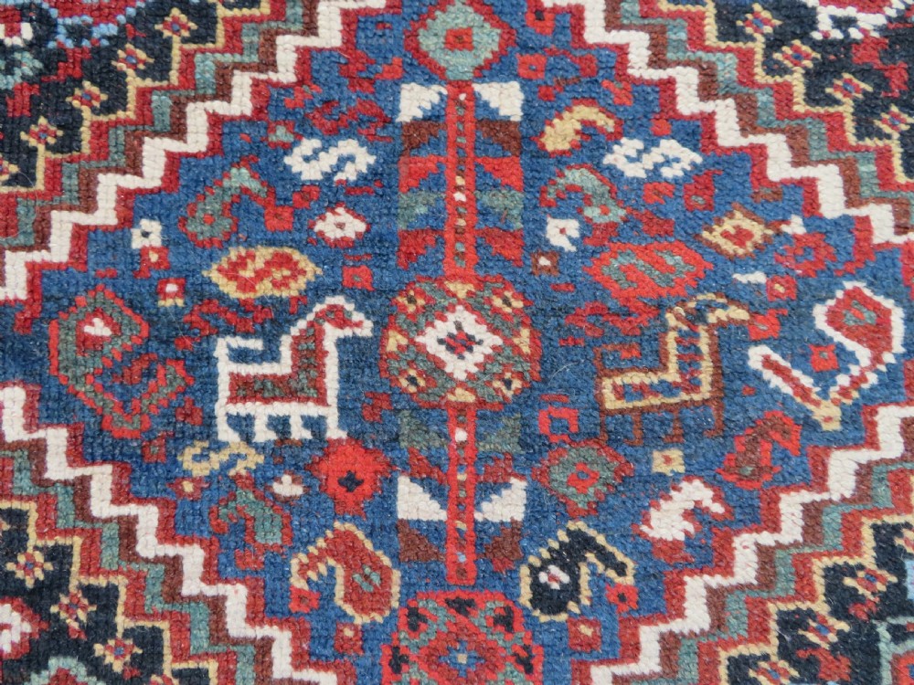 An antique South West Persian Khamseh wool rug with repeating geometric diamond medallions in deep red and indigo blue tones. View VI