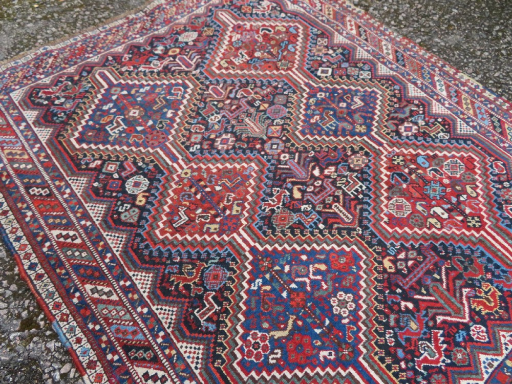 An antique South West Persian Khamseh wool rug with repeating geometric diamond medallions in deep red and indigo blue tones. View VIII