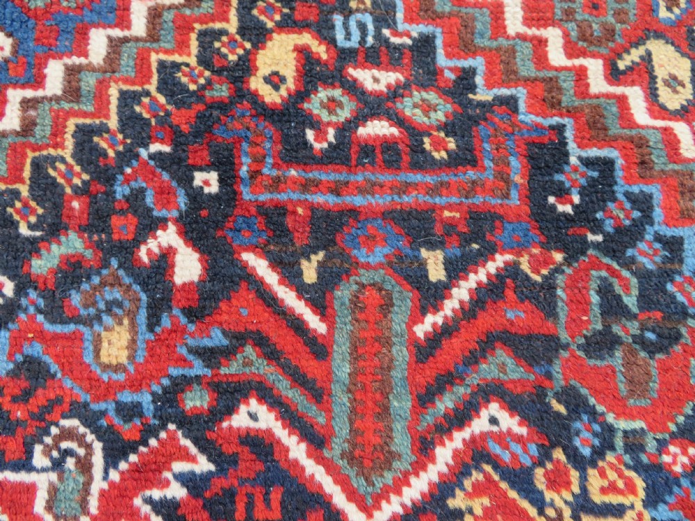 An antique South West Persian Khamseh wool rug with repeating geometric diamond medallions in deep red and indigo blue tones. View X