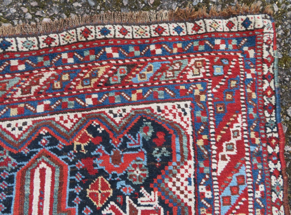 An antique South West Persian Khamseh wool rug with repeating geometric diamond medallions in deep red and indigo blue tones. View XI