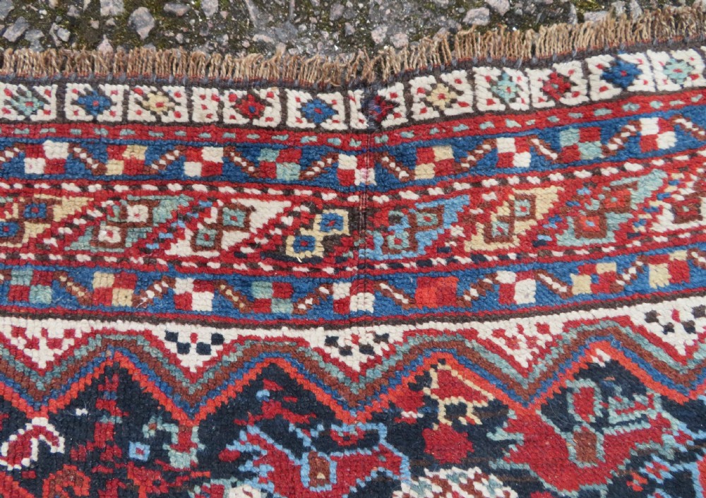 An antique South West Persian Khamseh wool rug with repeating geometric diamond medallions in deep red and indigo blue tones. View XII