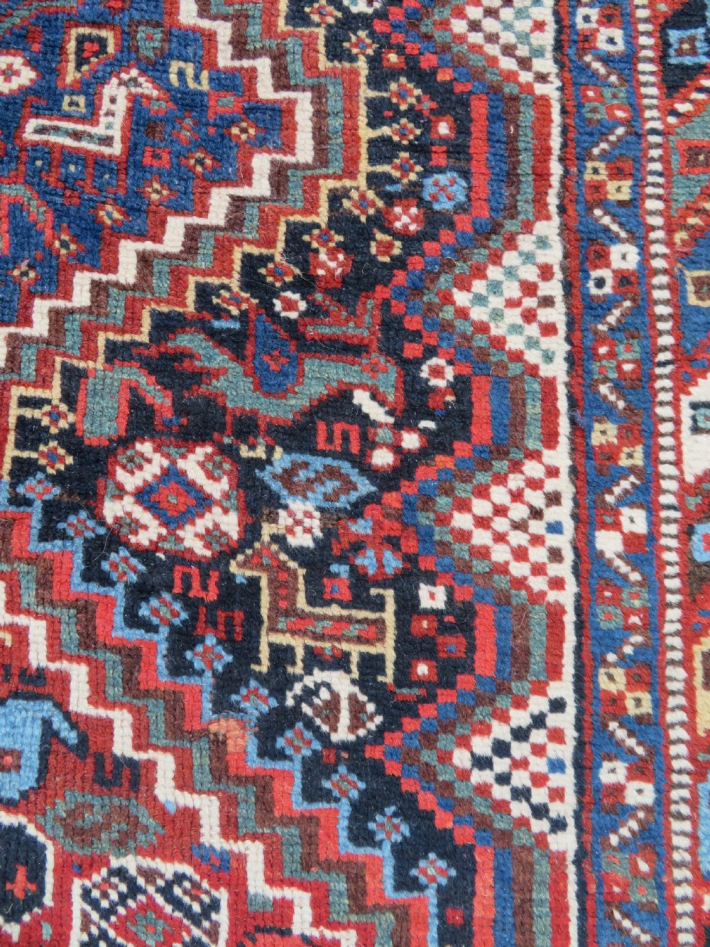 An antique South West Persian Khamseh wool rug with repeating geometric diamond medallions in deep red and indigo blue tones. View XIII
