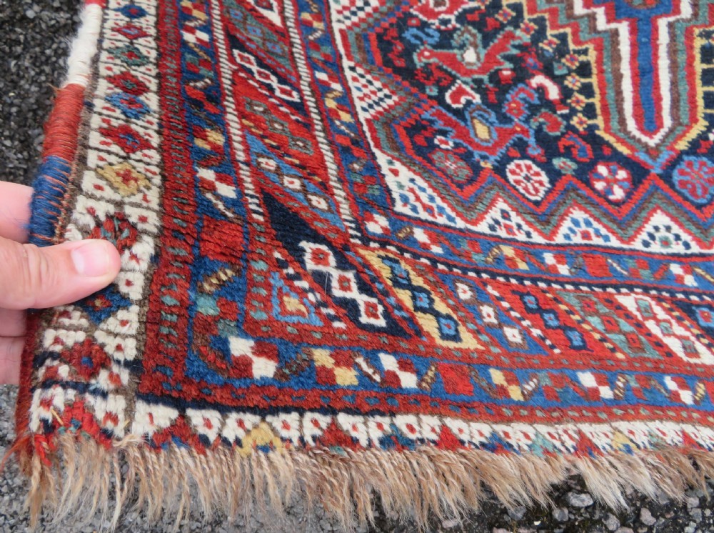 An antique South West Persian Khamseh wool rug with repeating geometric diamond medallions in deep red and indigo blue tones. View XVI