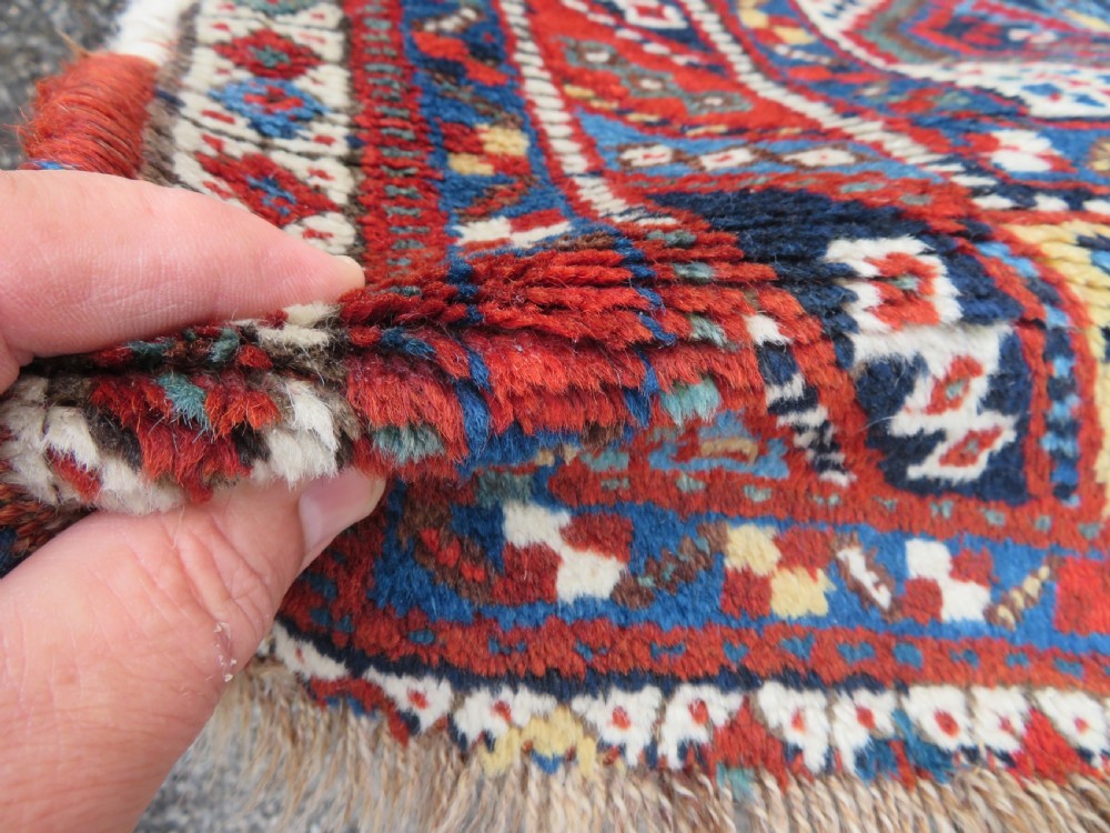 An antique South West Persian Khamseh wool rug with repeating geometric diamond medallions in deep red and indigo blue tones. View XVII