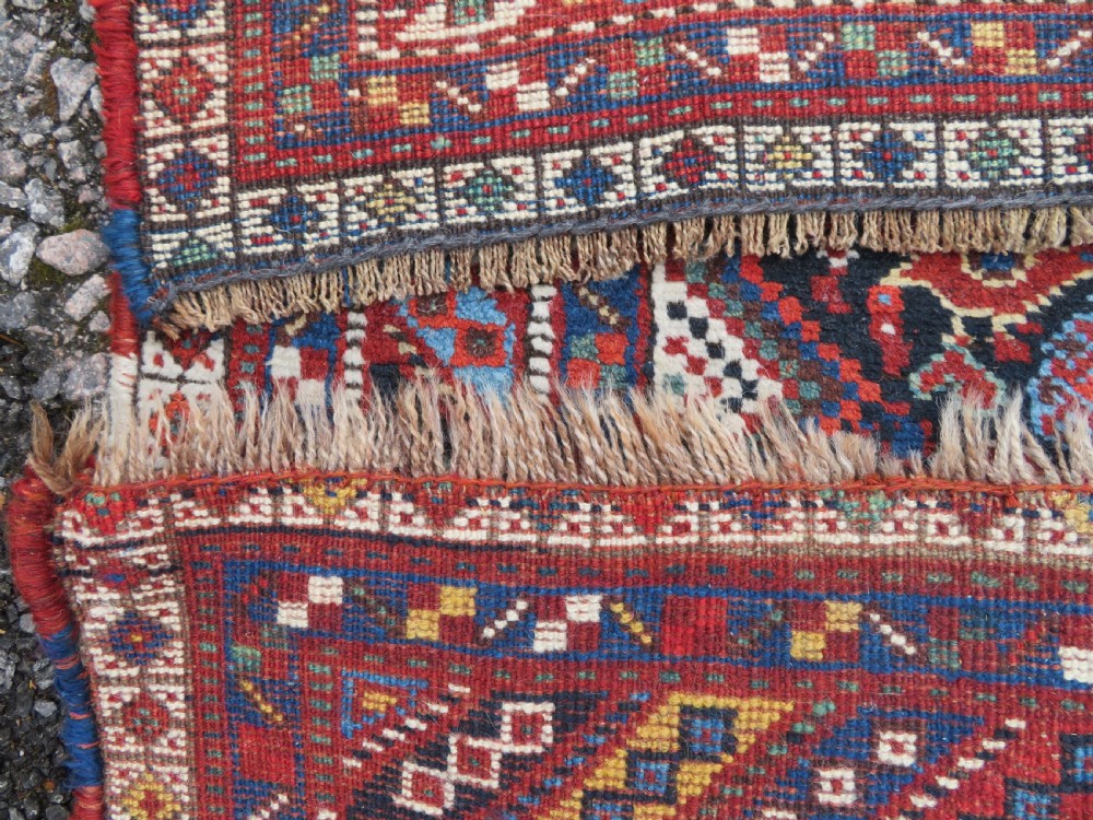 An antique South West Persian Khamseh wool rug with repeating geometric diamond medallions in deep red and indigo blue tones. View XIX