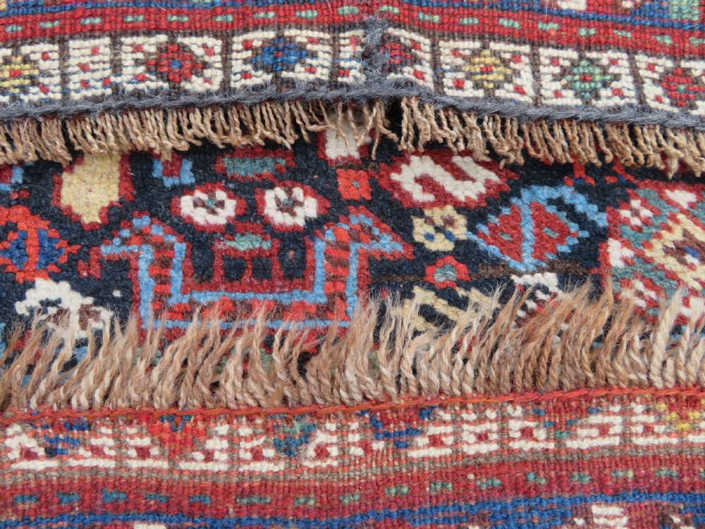 An antique South West Persian Khamseh wool rug with repeating geometric diamond medallions in deep red and indigo blue tones. View XX