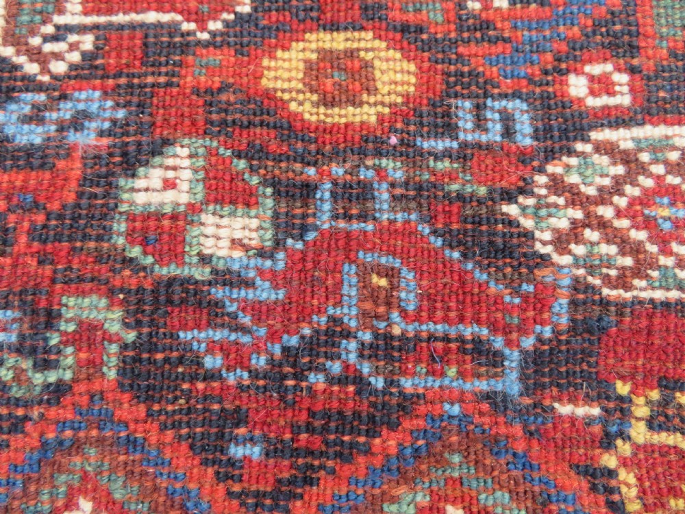 An antique South West Persian Khamseh wool rug with repeating geometric diamond medallions in deep red and indigo blue tones. View XXI