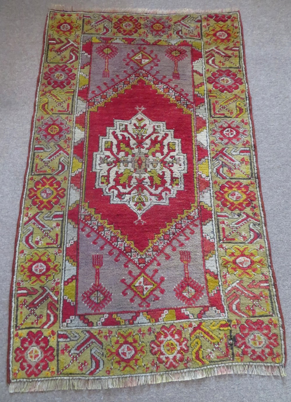 An early 19th-century Central Anatolian Konya rug featuring a central red field with a stepped diamond medallion surrounded by mustard-yellow geometric borders. View IV