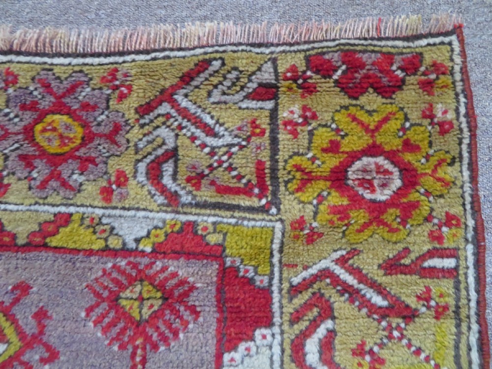 An early 19th-century Central Anatolian Konya rug featuring a central red field with a stepped diamond medallion surrounded by mustard-yellow geometric borders. View V