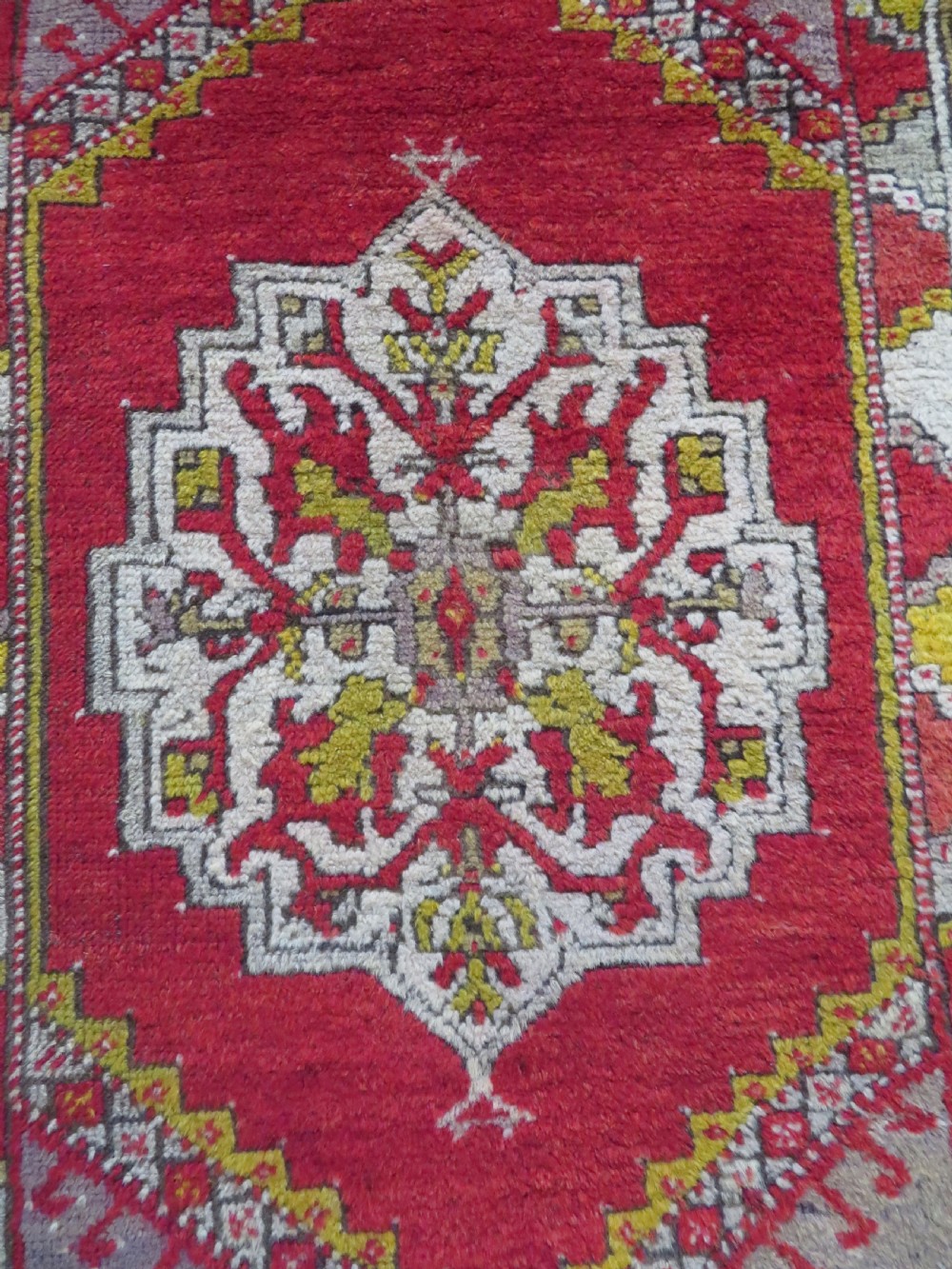 An early 19th-century Central Anatolian Konya rug featuring a central red field with a stepped diamond medallion surrounded by mustard-yellow geometric borders. View VI
