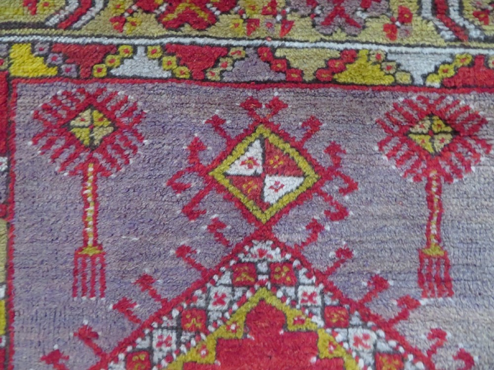 An early 19th-century Central Anatolian Konya rug featuring a central red field with a stepped diamond medallion surrounded by mustard-yellow geometric borders. View VII