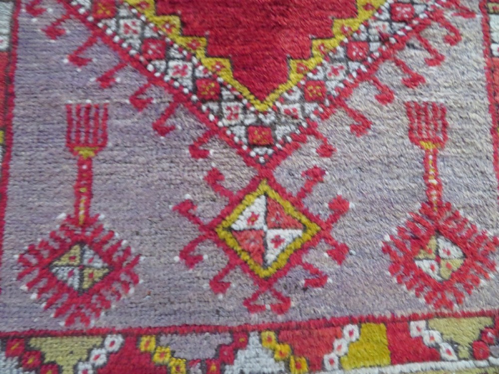 An early 19th-century Central Anatolian Konya rug featuring a central red field with a stepped diamond medallion surrounded by mustard-yellow geometric borders. View X