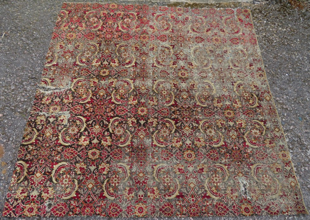 A square-shaped North Indian Mughal wool carpet fragment featuring detailed crimson and dark brown floral scrollwork.