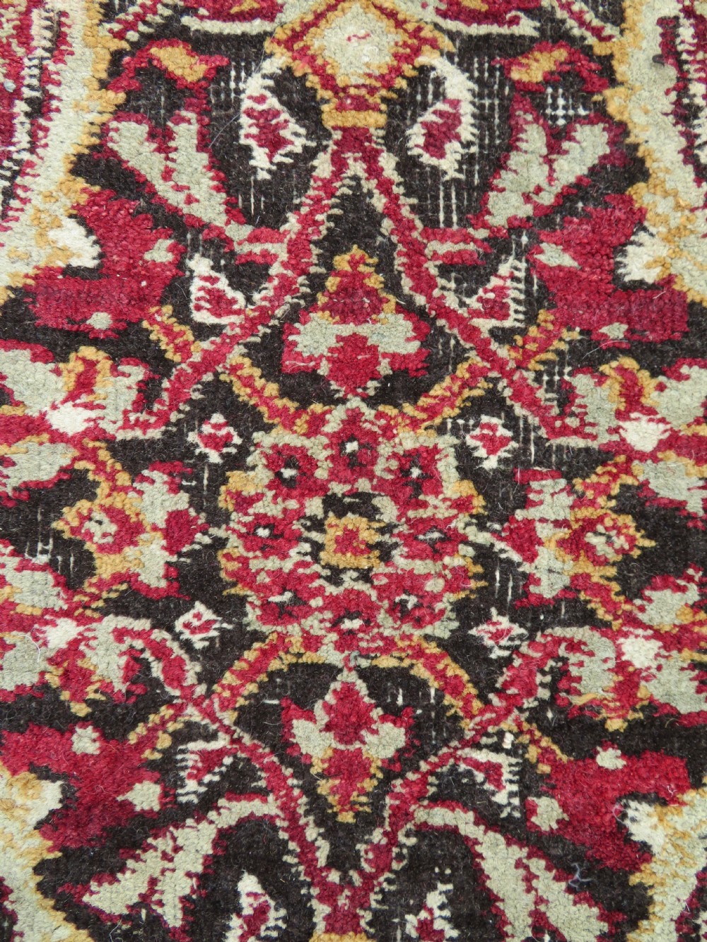 A square-shaped North Indian Mughal wool carpet fragment featuring detailed crimson and dark brown floral scrollwork. View V