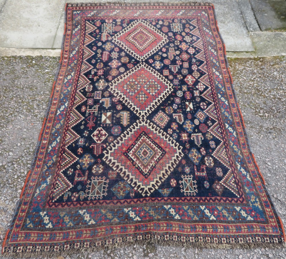 An antique hand-knotted Luri wool rug featuring three central diamond medallions surrounded by geometric tribal symbols on a dark navy field with a red border.