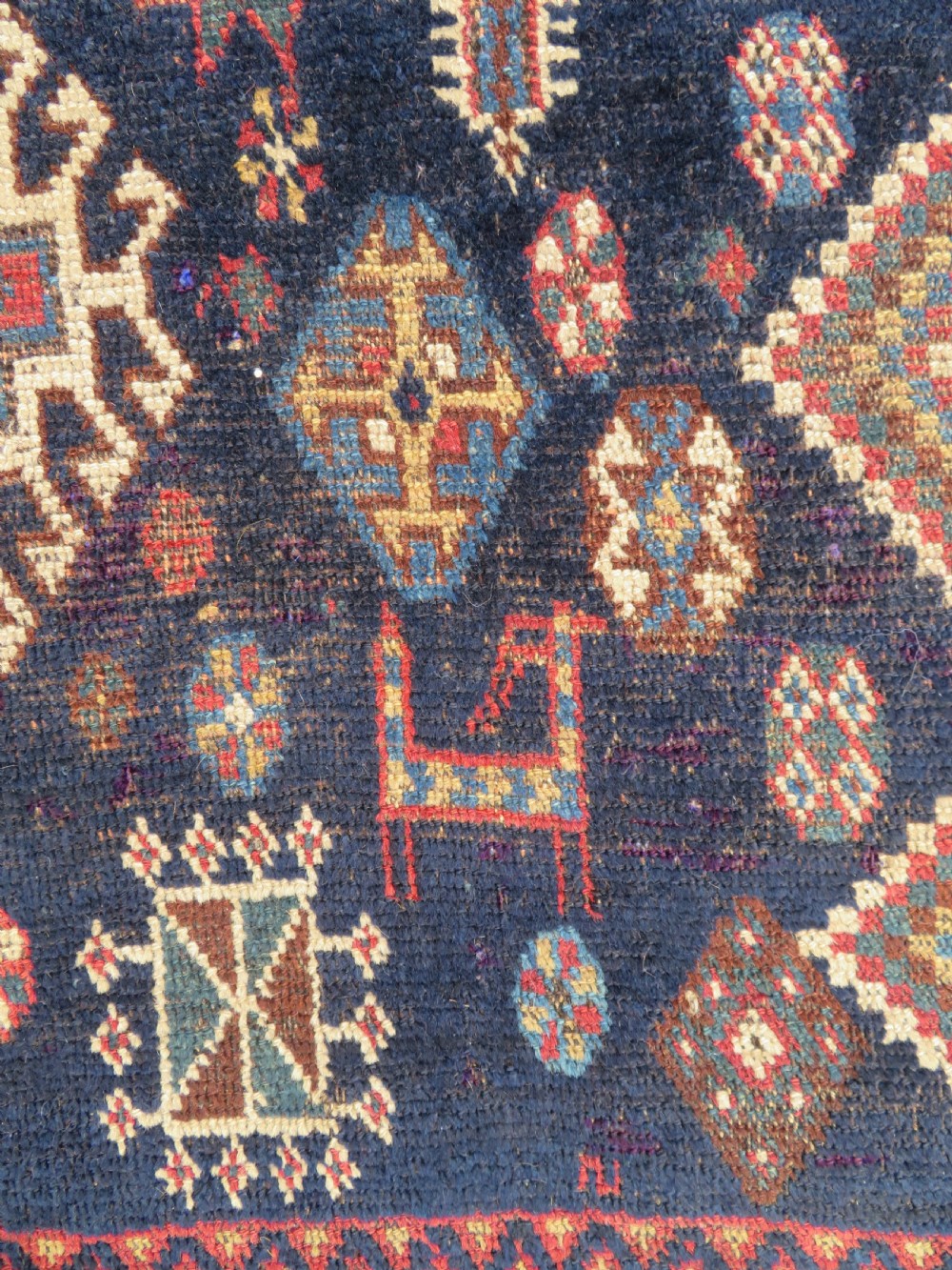 An antique hand-knotted Luri wool rug featuring three central diamond medallions surrounded by geometric tribal symbols on a dark navy field with a red border. View V