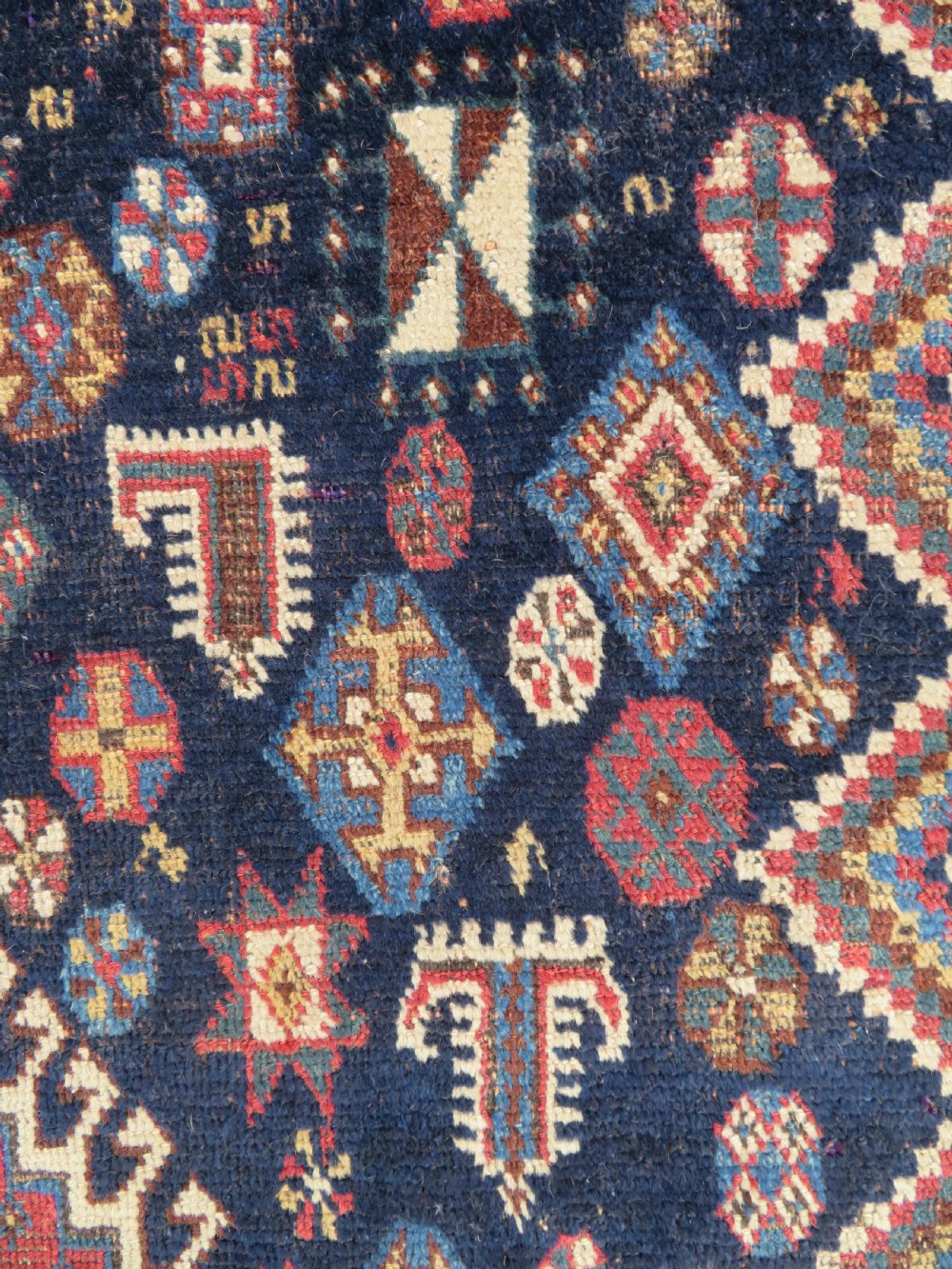 An antique hand-knotted Luri wool rug featuring three central diamond medallions surrounded by geometric tribal symbols on a dark navy field with a red border. View VI