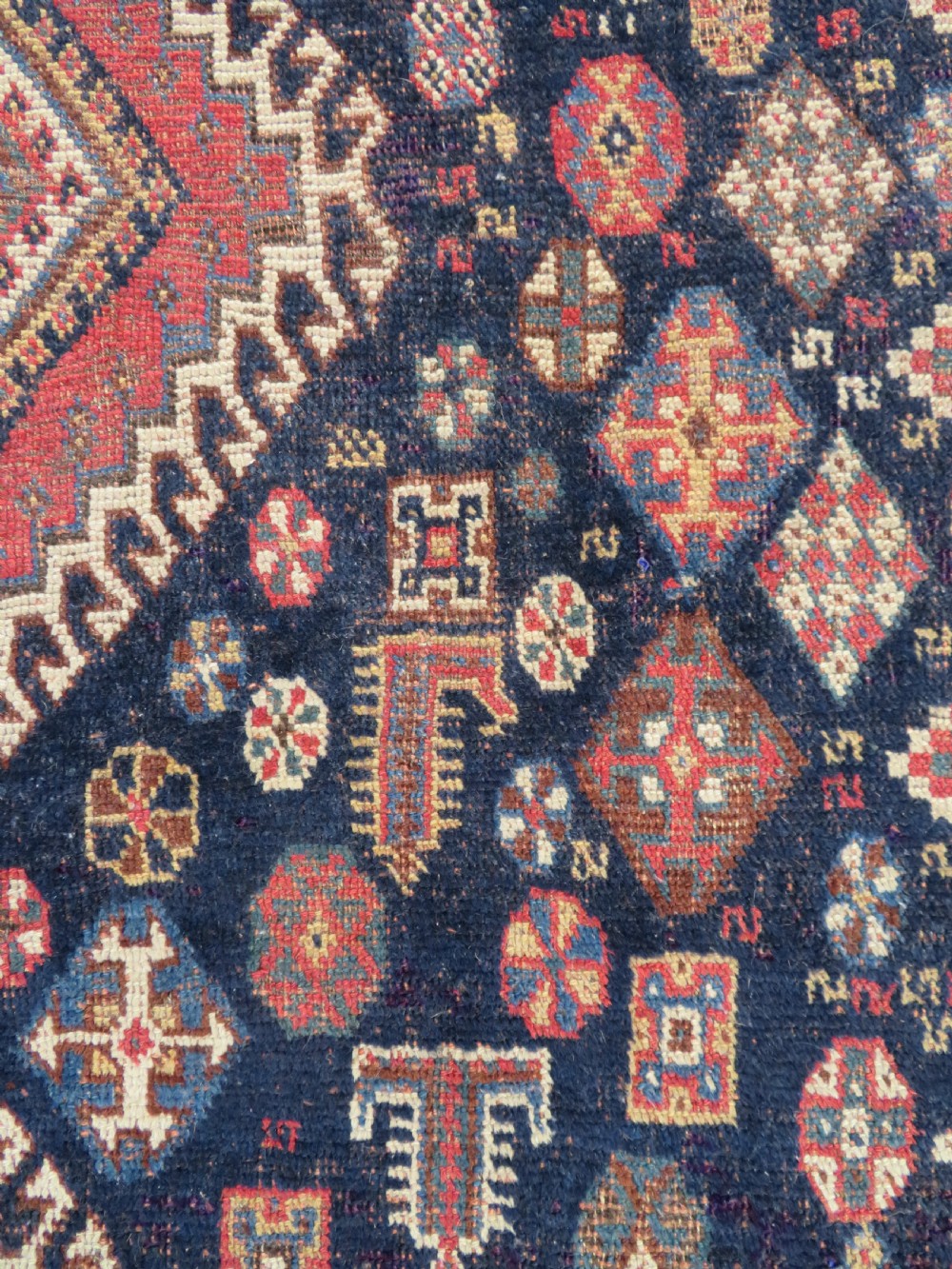 An antique hand-knotted Luri wool rug featuring three central diamond medallions surrounded by geometric tribal symbols on a dark navy field with a red border. View VII