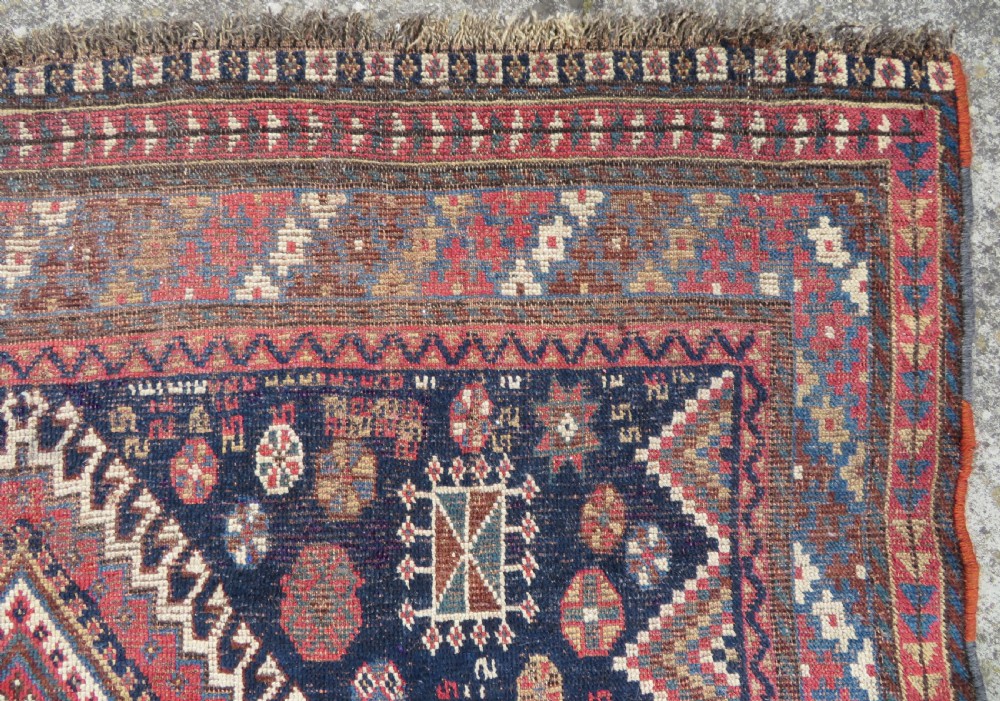 An antique hand-knotted Luri wool rug featuring three central diamond medallions surrounded by geometric tribal symbols on a dark navy field with a red border. View VIII