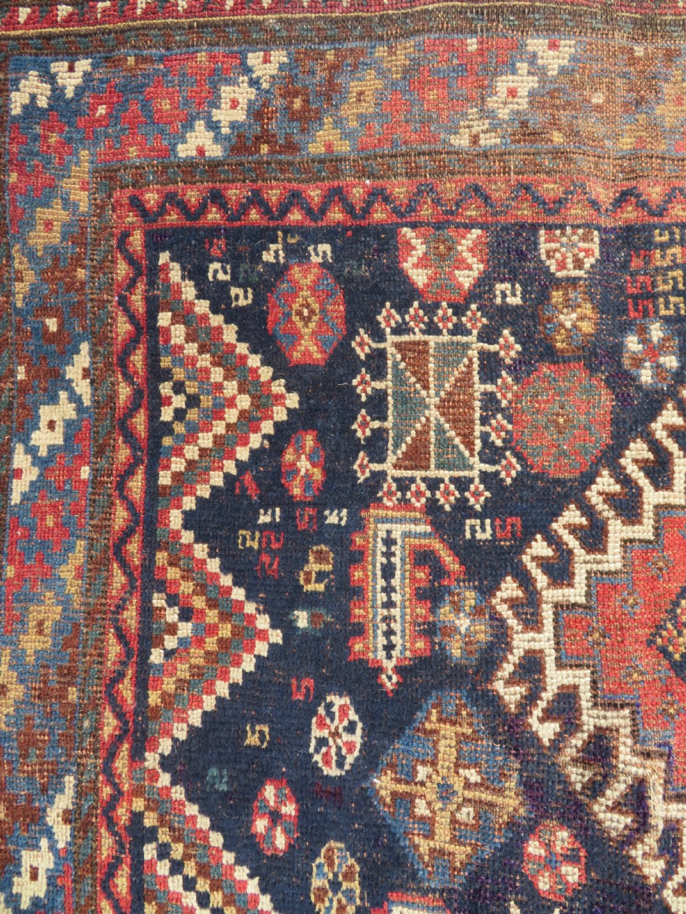An antique hand-knotted Luri wool rug featuring three central diamond medallions surrounded by geometric tribal symbols on a dark navy field with a red border. View IX