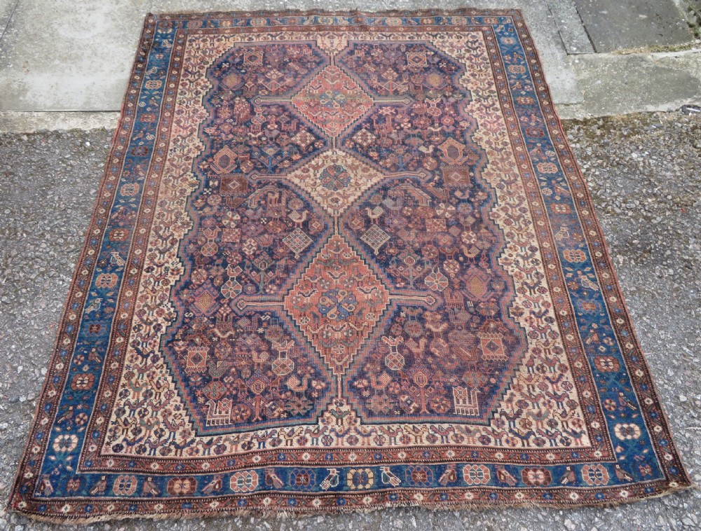 A hand-knotted antique Khamseh wool rug featuring three stepped diamond medallions surrounded by dense floral and avian tribal motifs on a dark navy blue field with multi-tiered geometric borders.