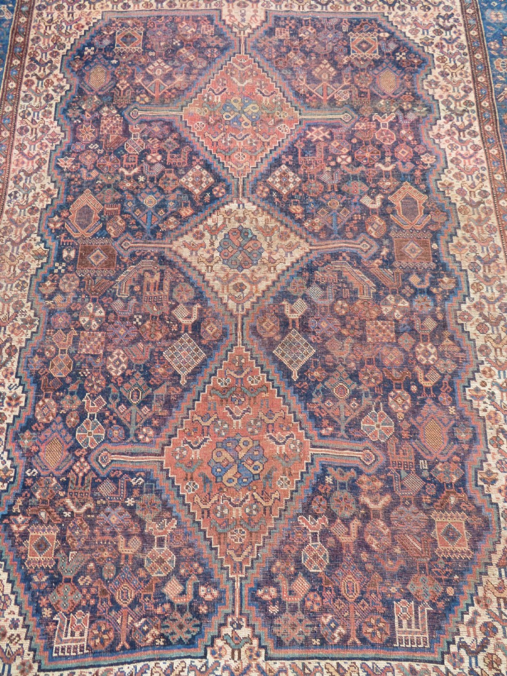 A hand-knotted antique Khamseh wool rug featuring three stepped diamond medallions surrounded by dense floral and avian tribal motifs on a dark navy blue field with multi-tiered geometric borders. View IV