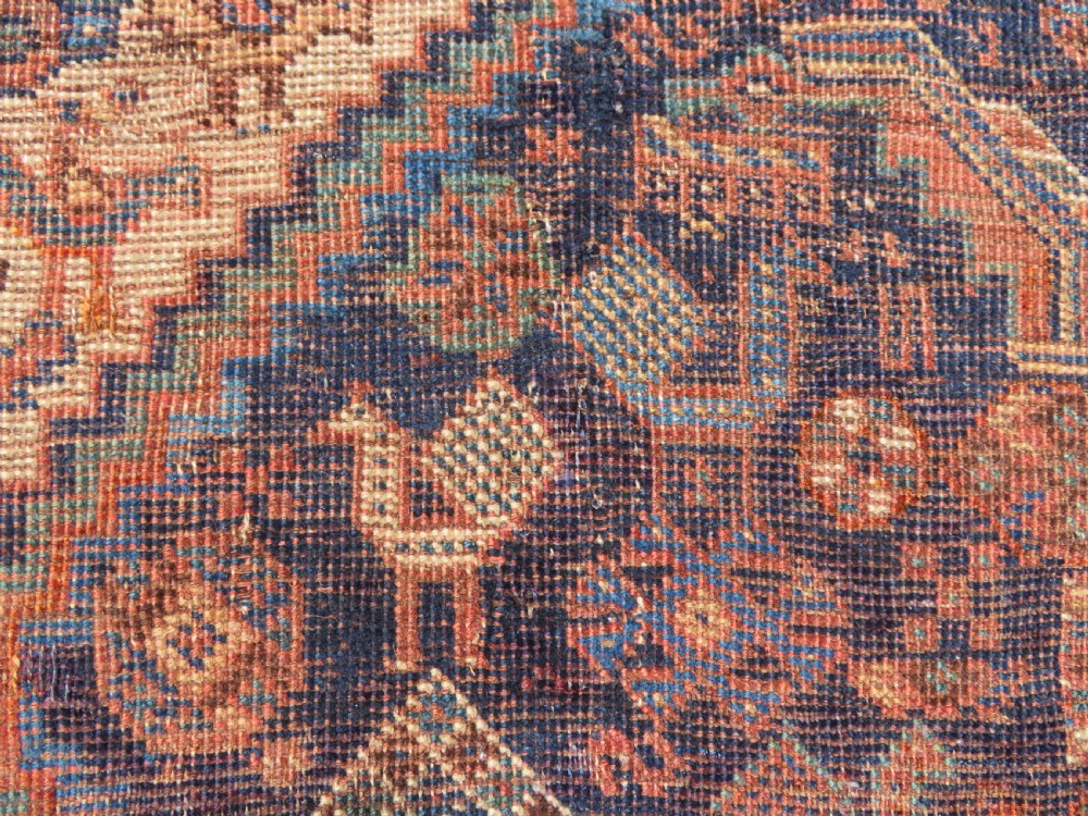 A hand-knotted antique Khamseh wool rug featuring three stepped diamond medallions surrounded by dense floral and avian tribal motifs on a dark navy blue field with multi-tiered geometric borders. View V