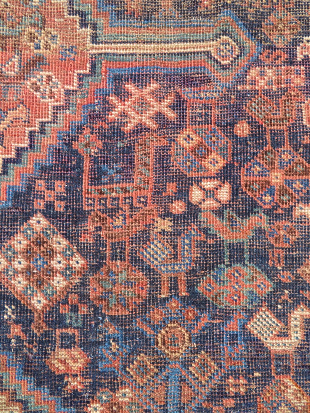 A hand-knotted antique Khamseh wool rug featuring three stepped diamond medallions surrounded by dense floral and avian tribal motifs on a dark navy blue field with multi-tiered geometric borders. View VI