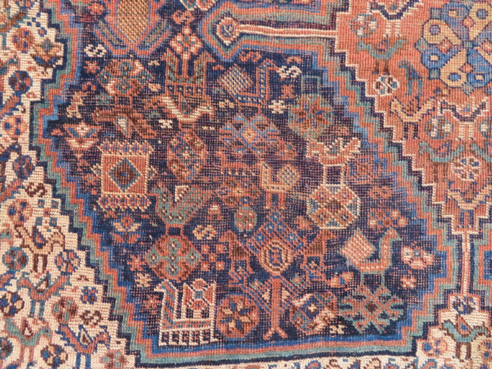 A hand-knotted antique Khamseh wool rug featuring three stepped diamond medallions surrounded by dense floral and avian tribal motifs on a dark navy blue field with multi-tiered geometric borders. View X