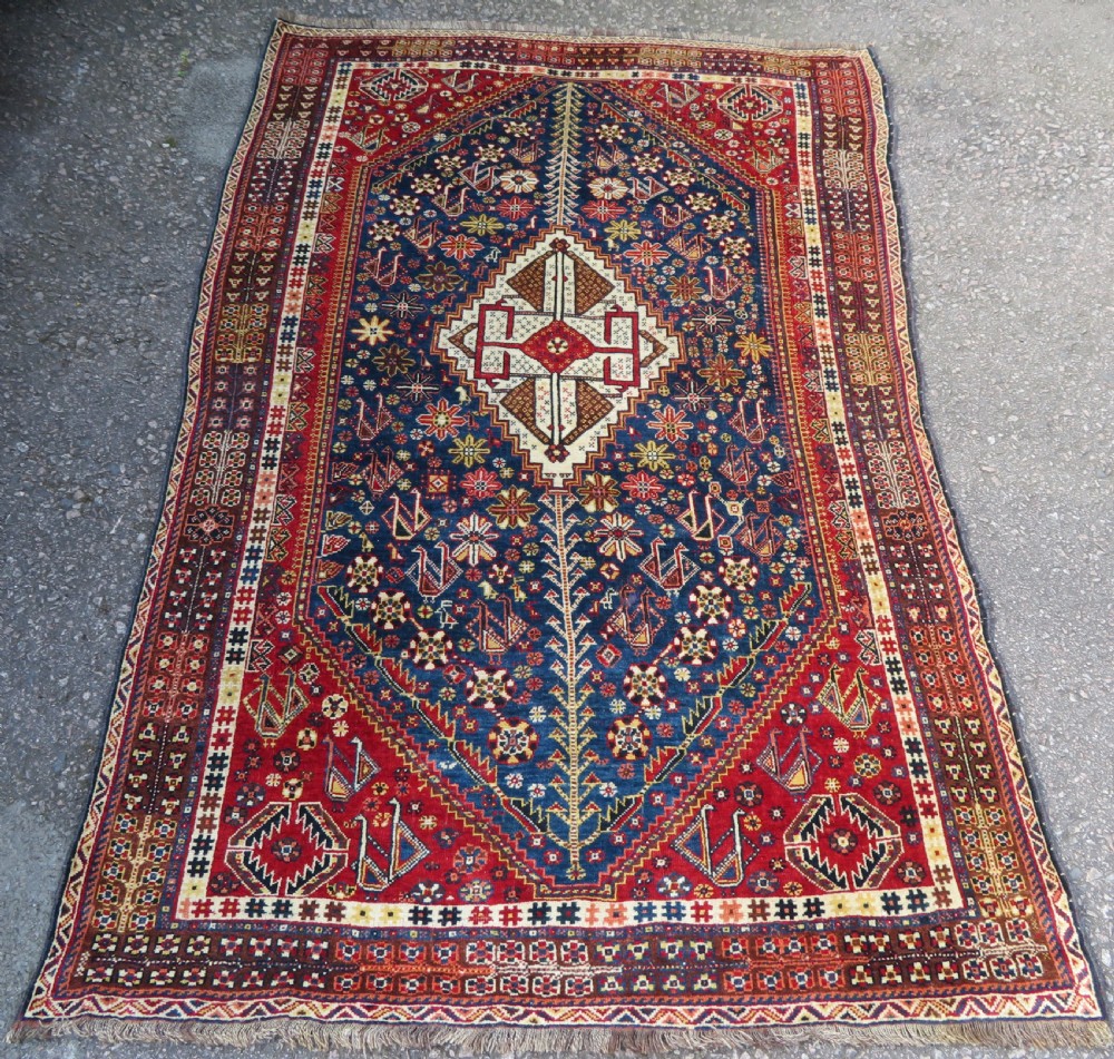 An antique Qashqai tribal wool rug featuring a deep blue central field with geometric bird motifs, red spandrels, and a complex multi-band border.
