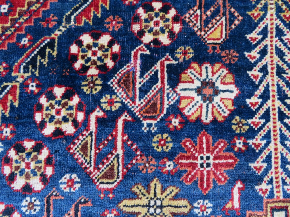 An antique Qashqai tribal wool rug featuring a deep blue central field with geometric bird motifs, red spandrels, and a complex multi-band border. View IV