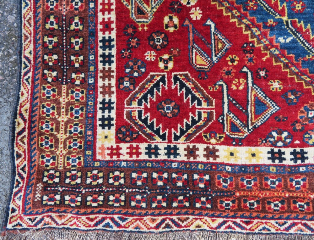 An antique Qashqai tribal wool rug featuring a deep blue central field with geometric bird motifs, red spandrels, and a complex multi-band border. View VII