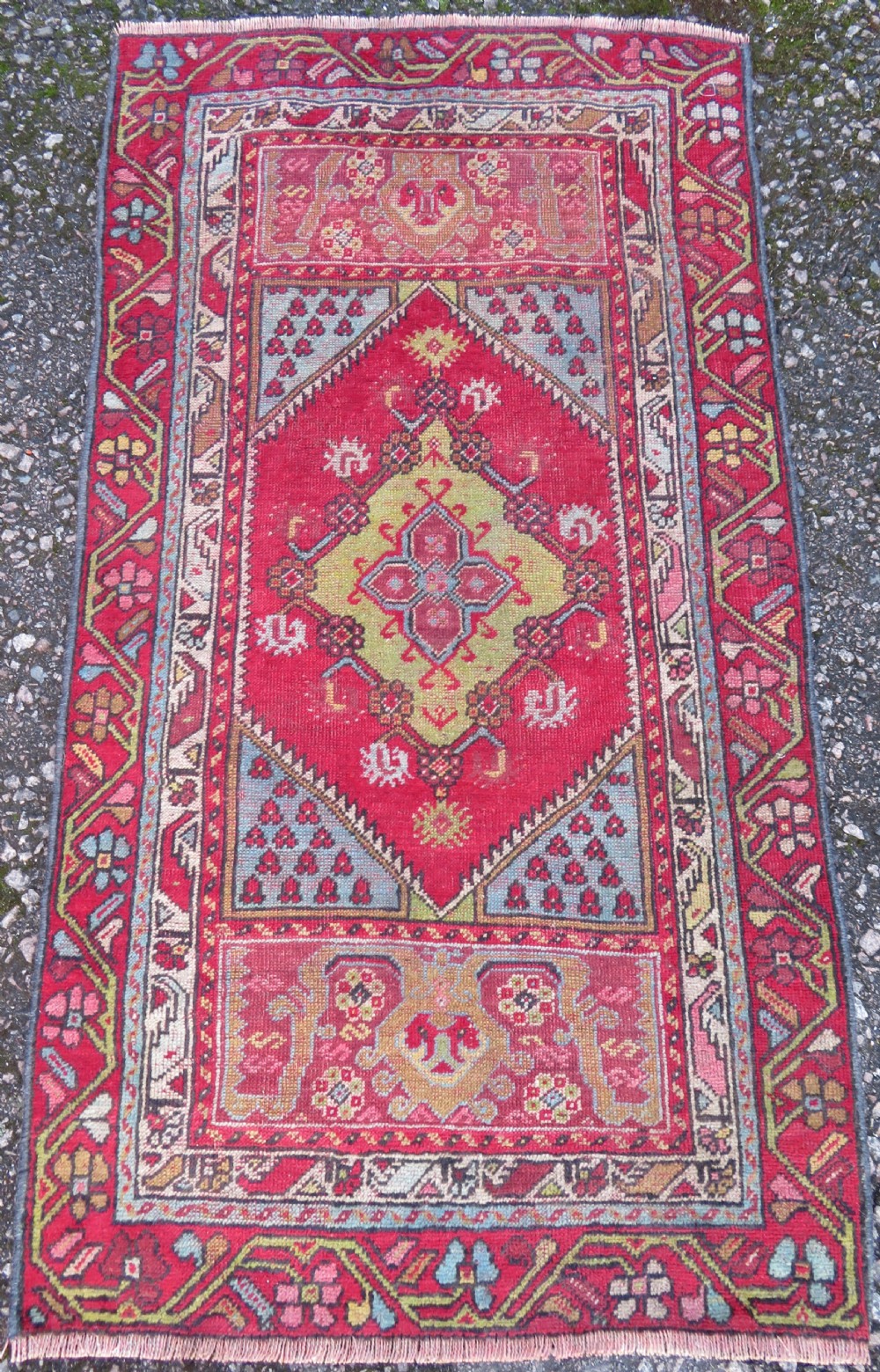 An antique hand-knotted Anatolian wool rug featuring a bold red field, a central geometric medallion in green and yellow, and detailed multi-patterned borders.