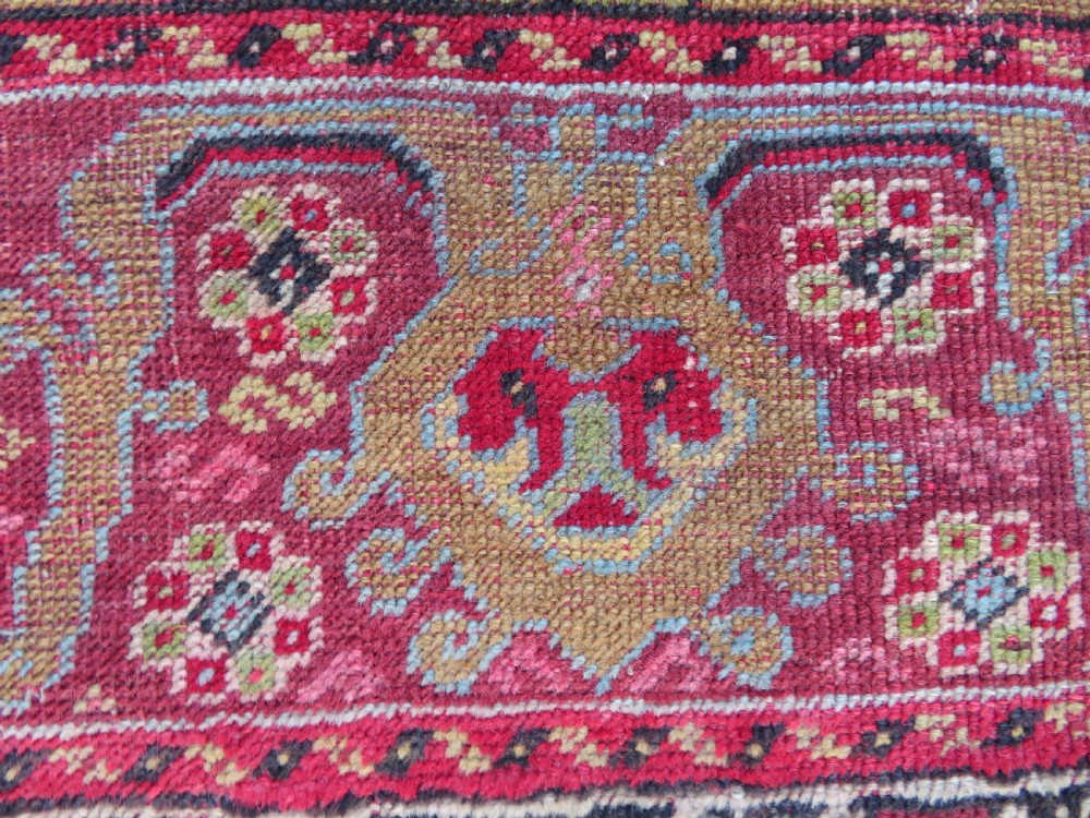 An antique hand-knotted Anatolian wool rug featuring a bold red field, a central geometric medallion in green and yellow, and detailed multi-patterned borders. View IX