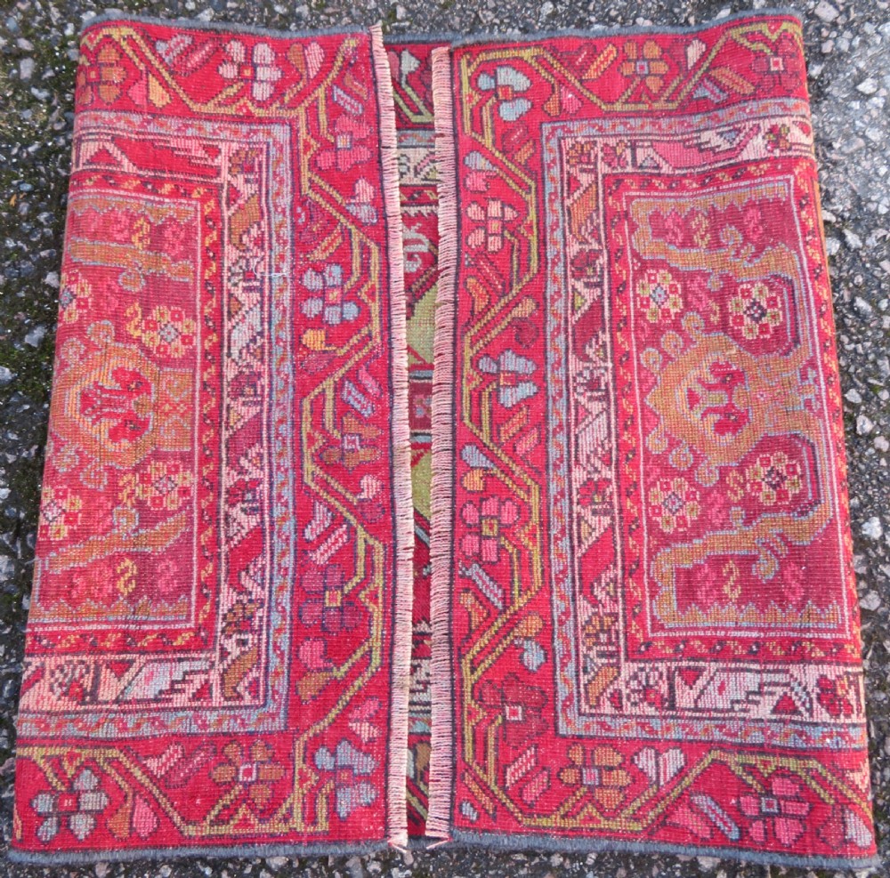 An antique hand-knotted Anatolian wool rug featuring a bold red field, a central geometric medallion in green and yellow, and detailed multi-patterned borders. View X