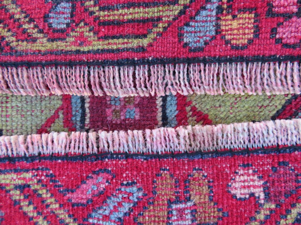 An antique hand-knotted Anatolian wool rug featuring a bold red field, a central geometric medallion in green and yellow, and detailed multi-patterned borders. View XI