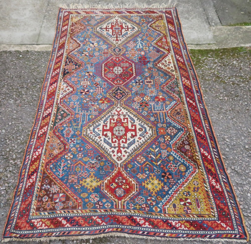 An antique hand-knotted Luri tribal rug featuring central diamond medallions on an indigo blue field framed by geometric red borders.