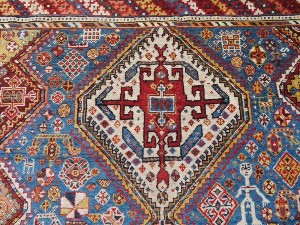 An antique hand-knotted Luri tribal rug featuring central diamond medallions on an indigo blue field framed by geometric red borders. View III