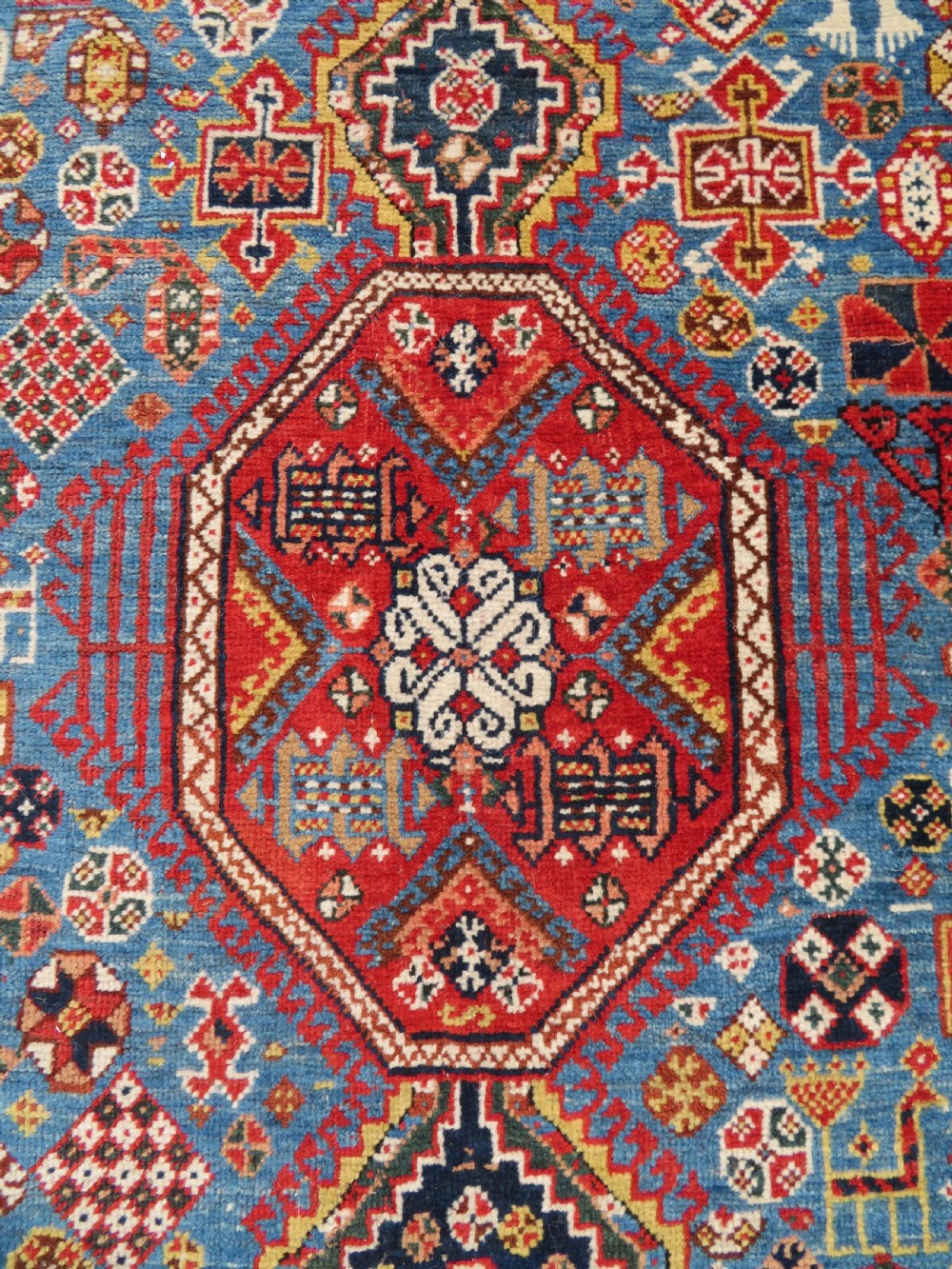 An antique hand-knotted Luri tribal rug featuring central diamond medallions on an indigo blue field framed by geometric red borders. View IV