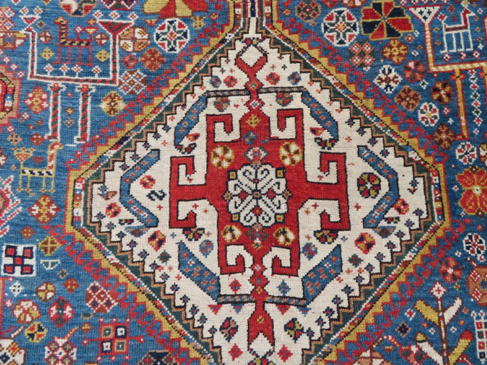 An antique hand-knotted Luri tribal rug featuring central diamond medallions on an indigo blue field framed by geometric red borders. View V