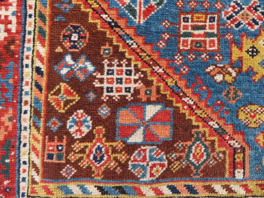 An antique hand-knotted Luri tribal rug featuring central diamond medallions on an indigo blue field framed by geometric red borders. View VI