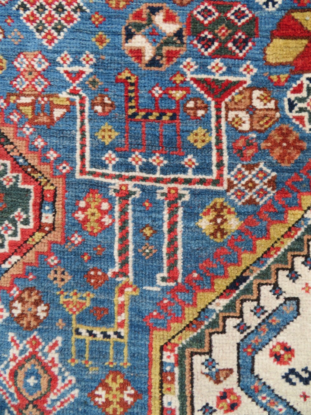 An antique hand-knotted Luri tribal rug featuring central diamond medallions on an indigo blue field framed by geometric red borders. View VII