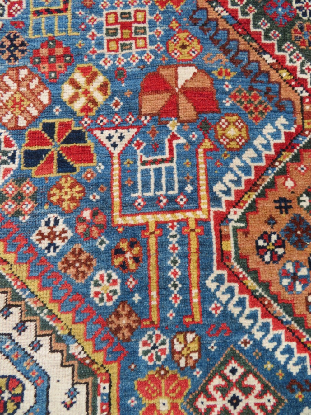 An antique hand-knotted Luri tribal rug featuring central diamond medallions on an indigo blue field framed by geometric red borders. View VIII