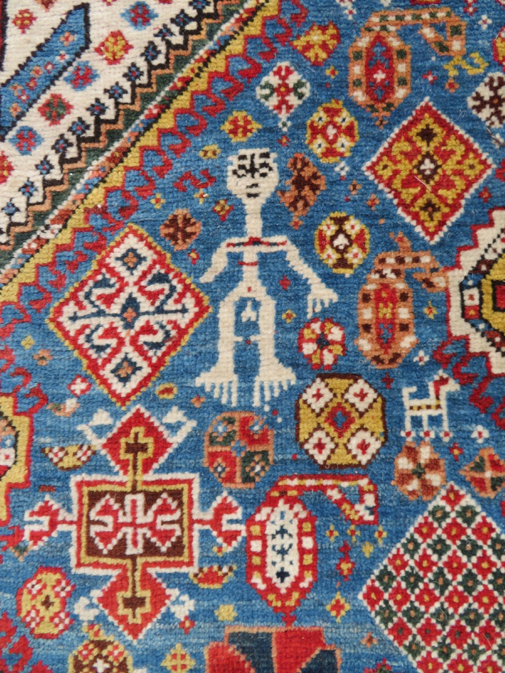 An antique hand-knotted Luri tribal rug featuring central diamond medallions on an indigo blue field framed by geometric red borders. View X