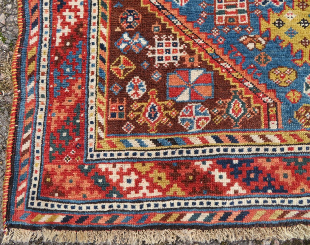 An antique hand-knotted Luri tribal rug featuring central diamond medallions on an indigo blue field framed by geometric red borders. View XIV