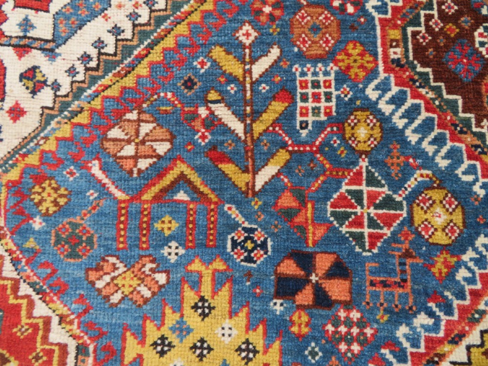 An antique hand-knotted Luri tribal rug featuring central diamond medallions on an indigo blue field framed by geometric red borders. View XIX