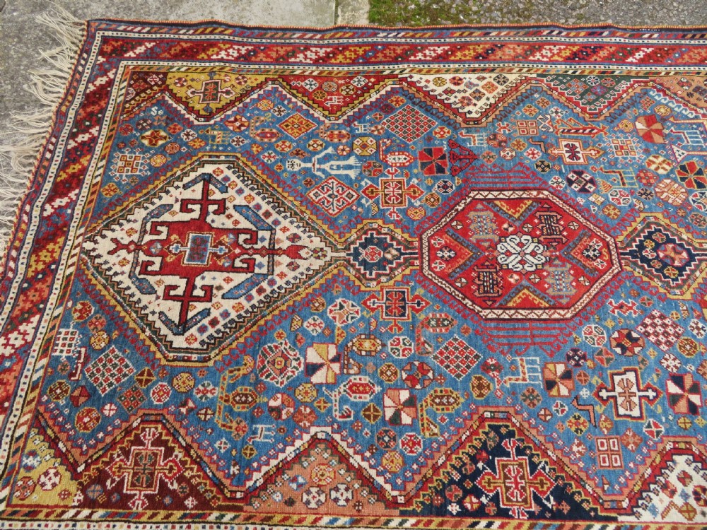 An antique hand-knotted Luri tribal rug featuring central diamond medallions on an indigo blue field framed by geometric red borders. View XX