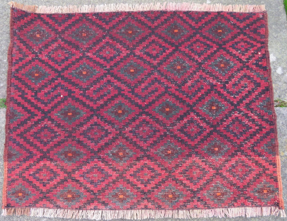 A square antique hand-knotted wool saddlebag face featuring a repeating geometric diamond pattern in red, navy blue, teal, and orange tones with light-coloured fringes. View III