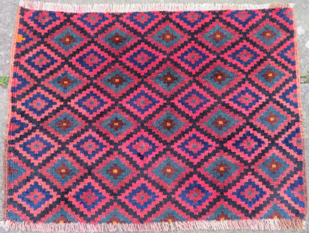 An antique hand-woven Luri saddle bag face featuring a repeating geometric diamond lattice pattern in shades of red, dark blue, cyan, and orange with fringed edges.