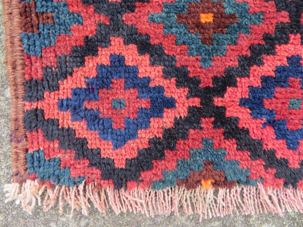 An antique hand-woven Luri saddle bag face featuring a repeating geometric diamond lattice pattern in shades of red, dark blue, cyan, and orange with fringed edges. View III